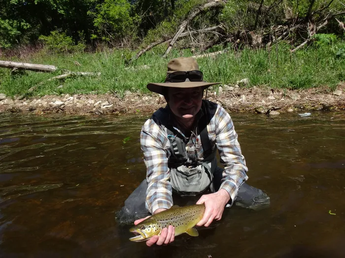 An angler in a summer river holding a brown trout before release