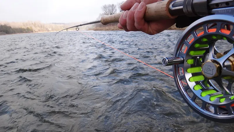 A fly reel and rod held low over the surface of a river, line running out across the current