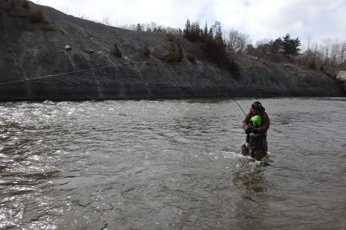 Two anglers wading the broad Lower Credit River below a shale cliff