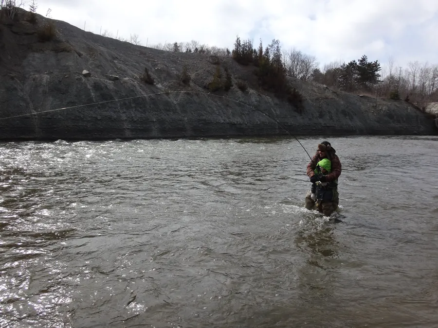 Two anglers wading a spring river, one with a float rod bent into a fish